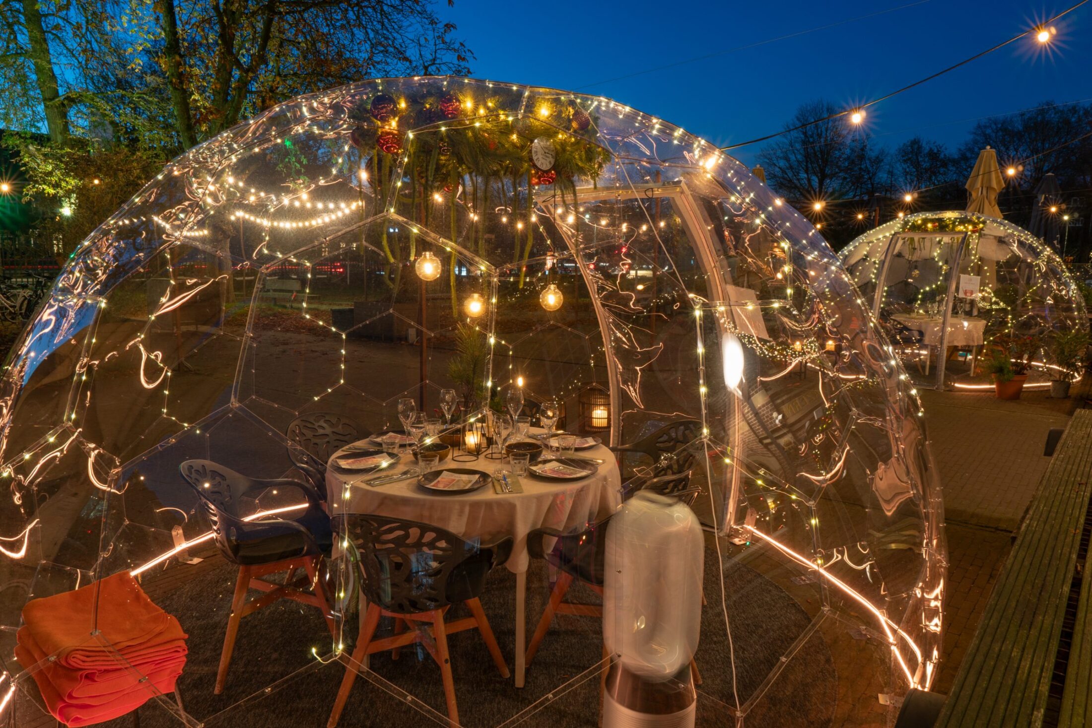 Gedekte tafel met wijnglazen in de verlichte dome in de tuin van In de Kazerne.
