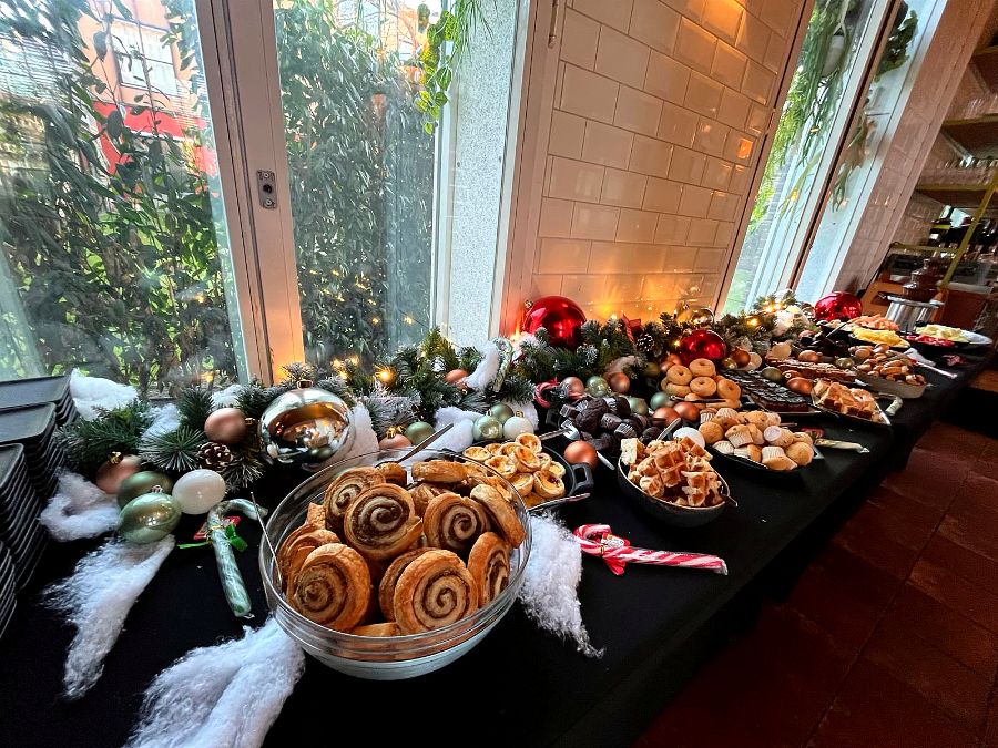 Lange dessertafel met kaneelbroodjes, wafels, soesjes en kerstballen voor de ramen.