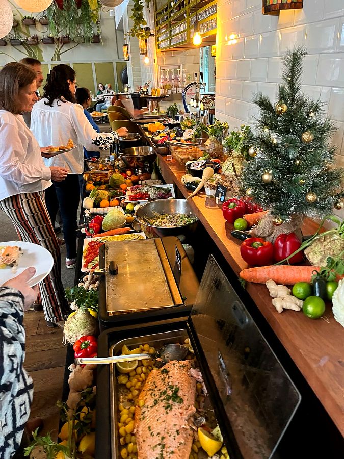 Gasten scheppen op aan het kerstbuffet met zalm, verse groenten en een kerstboompje op de bar.