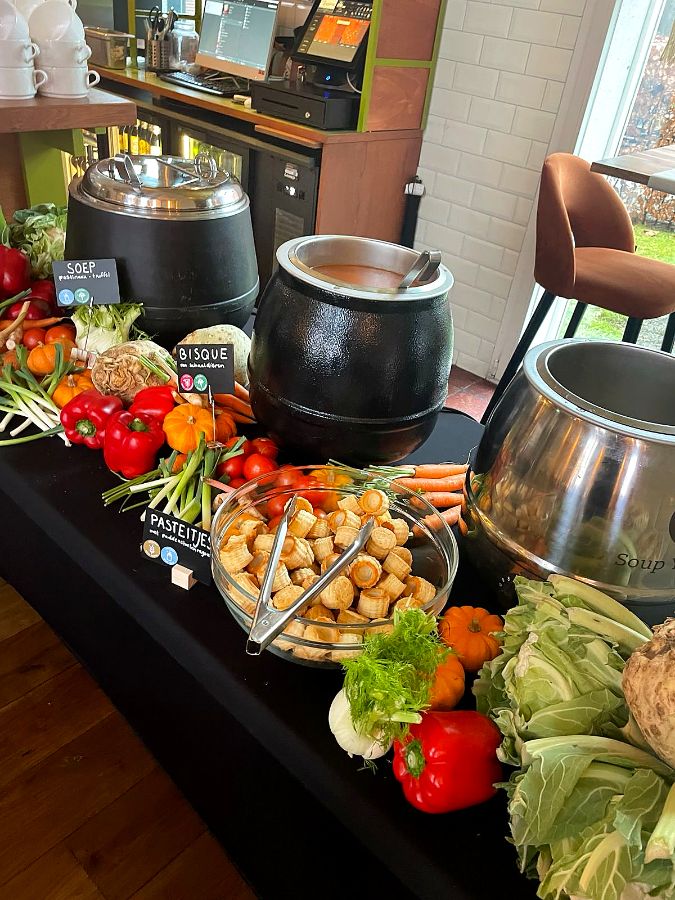 Soepketels met pastinaaksoep en bisque, pasteitjes en verse groenten op het buffet.