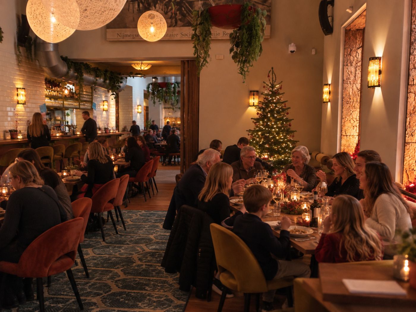 Familie aan een gedekte tafel met kaarslicht naast de verlichte kerstboom in In de Kazerne.