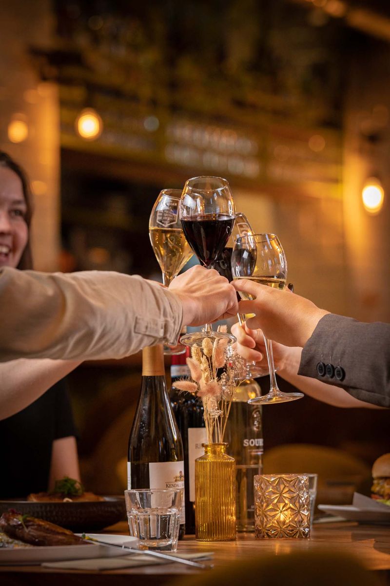 Gezelschap proost aan een gedekte tafel met wijn en kaarslicht in In de Kazerne.